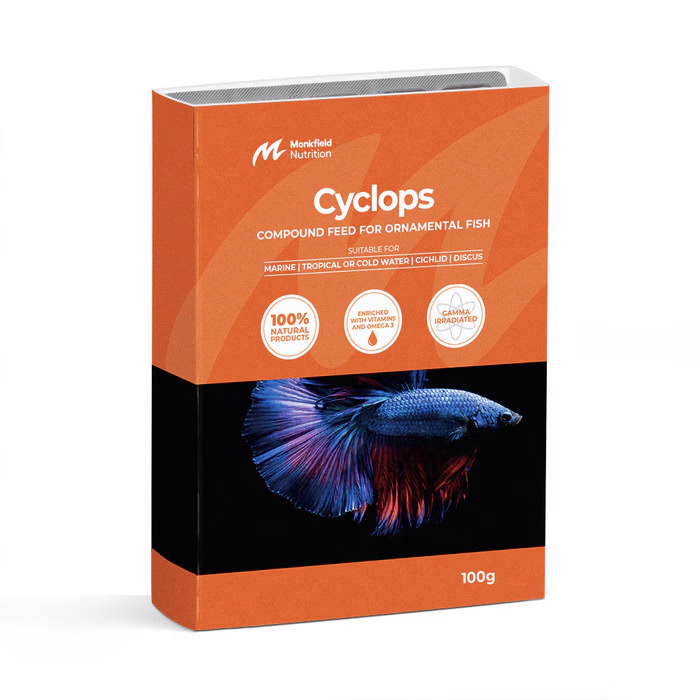 Packaging of Monkfield Nutrition Cyclops compound feed for ornamental fish, featuring an orange box with an image of small tropical fish swimming near aquatic plants, suitable for marine, cold, or freshwater fish, enriched with vitamins and omega-3, and gamma irradiated for safety